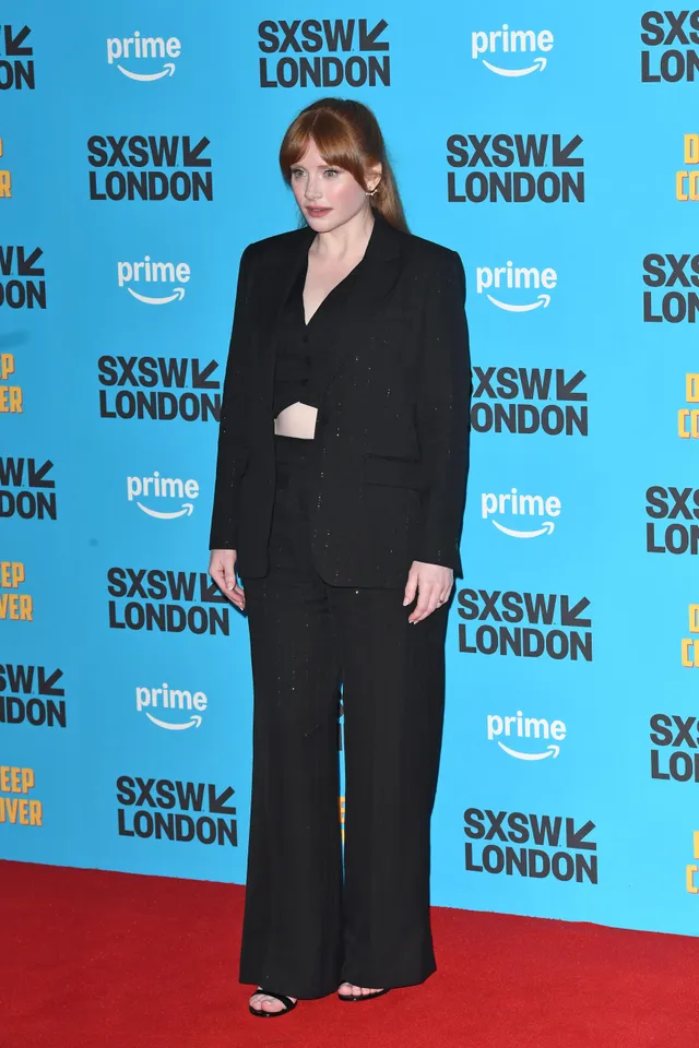 Bryce Dallas Howard standing at a premiere in a black tailored outfit.