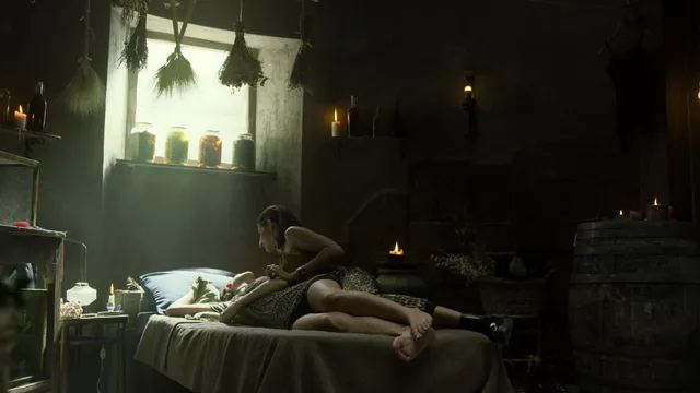 Úrsula Corberó reclining barefoot beside a man on a bed in a scene.