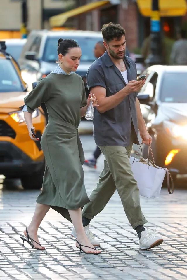 Daisy Ridley walking beside a man on a cobbled street.
