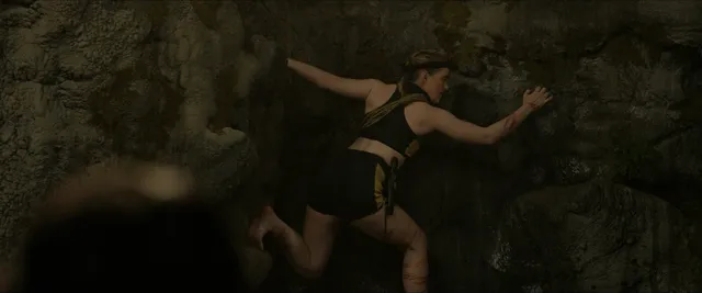 Kathryn Newton with her bare feet visible against rocks in a film scene.