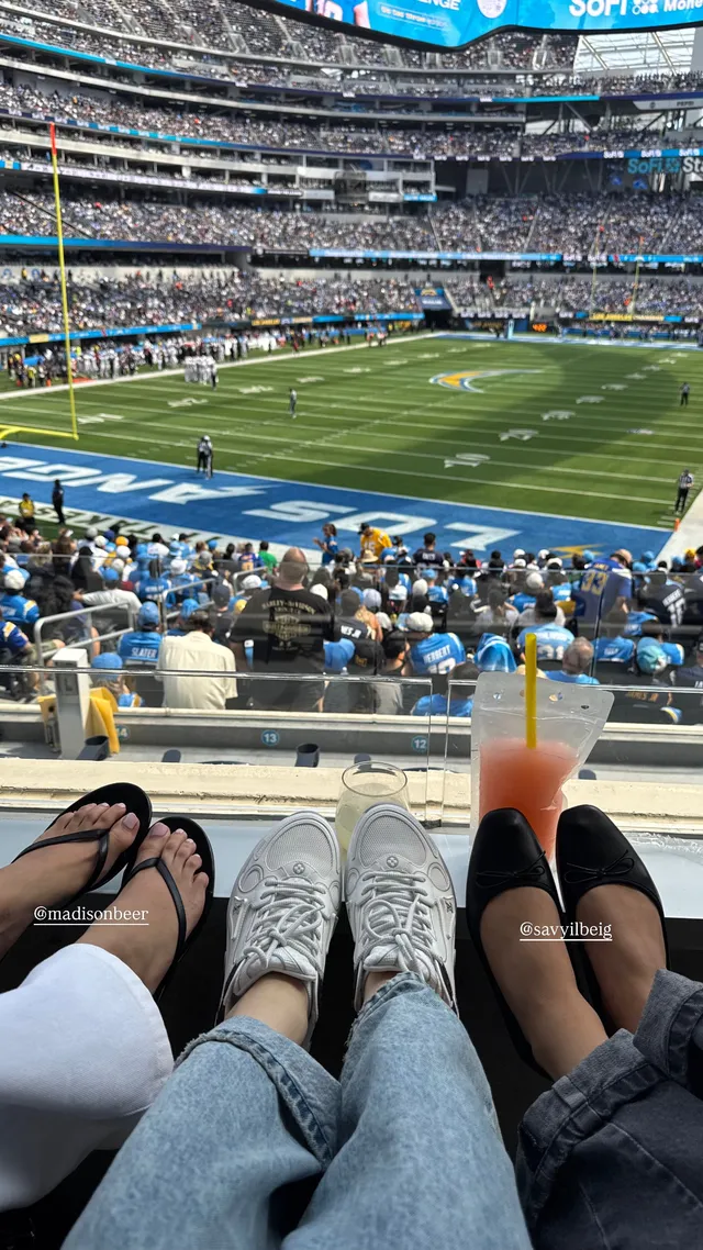 Madison Beer sitting beside companions at a sports stadium.