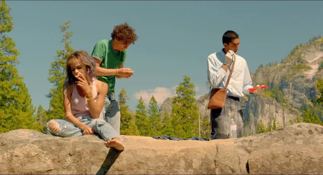 Zoë Kravitz sitting on a rock beside two men in a scene.