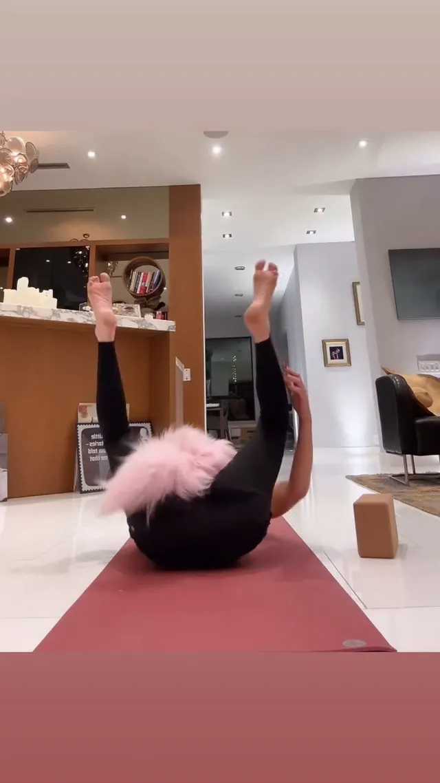 Kate Beckinsale rolling backward on an exercise mat with bare feet raised.