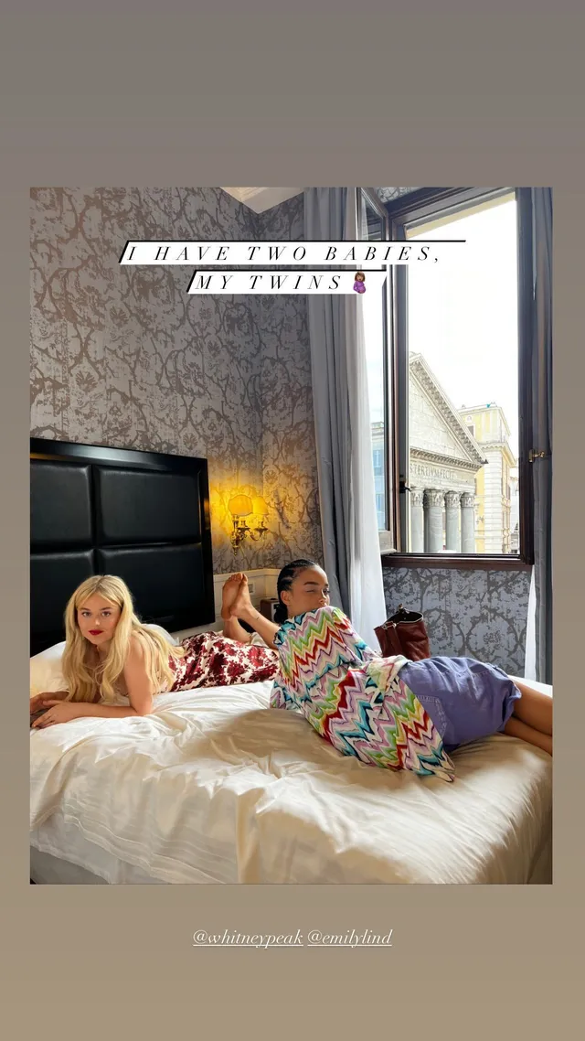 Emily Alyn Lind reclining barefoot beside a friend on a bed.
