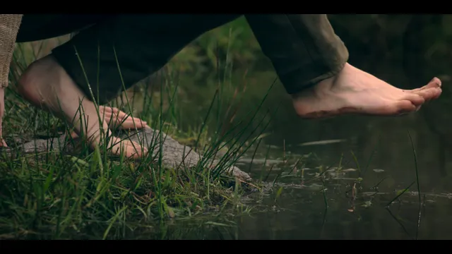 Freya Allan standing barefoot beside water in a film scene.