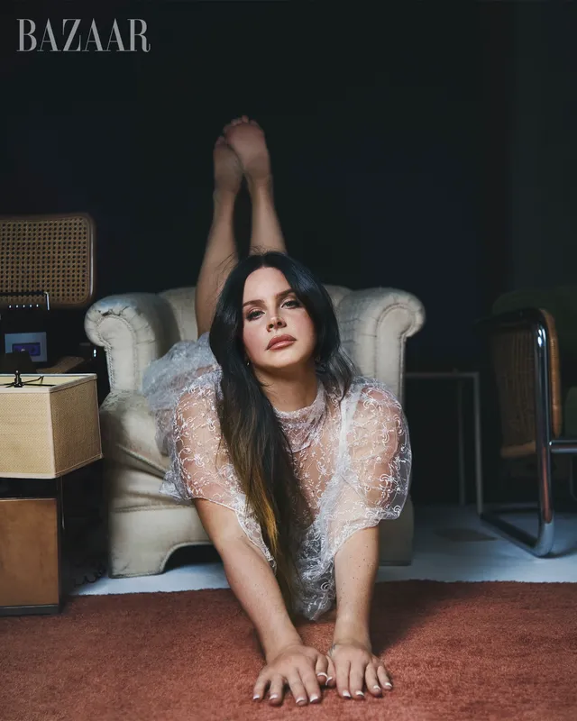 Lana Del Rey posing upside down in an armchair with her bare soles raised.