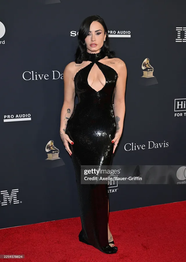 Demi Lovato standing on a red carpet in a black outfit and open-toe heels.