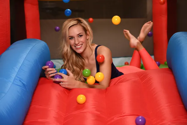 Paige Spiranac lying on an inflatable play structure with her bare feet raised while holding a toy.