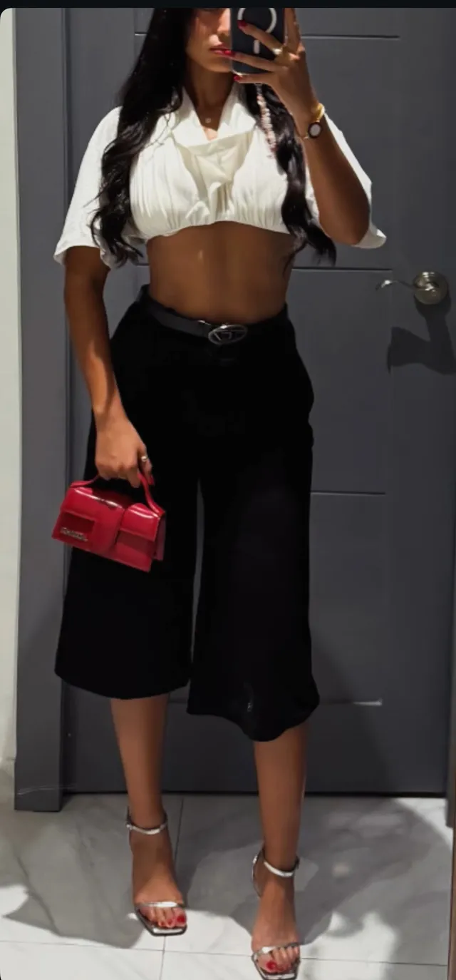 Emily Tosta wearing black trousers and silver heels for a mirror photograph.