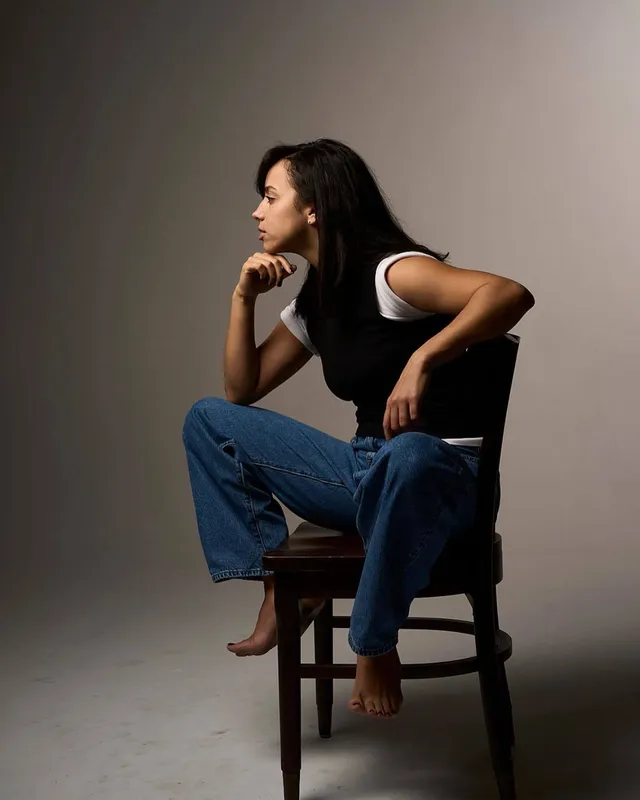 Kiana Madeira sitting barefoot on a chair in jeans and a dark top.