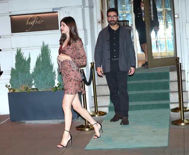 Alexandra Daddario walking outside in a patterned dress and heels.