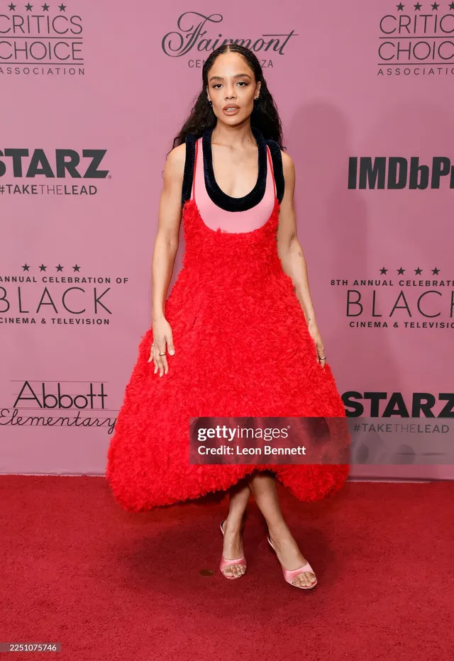 Tessa Thompson posing on a red carpet in a textured red dress.