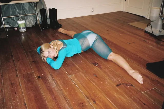 Addison Rae lying barefoot on a wooden floor in a turquoise outfit.