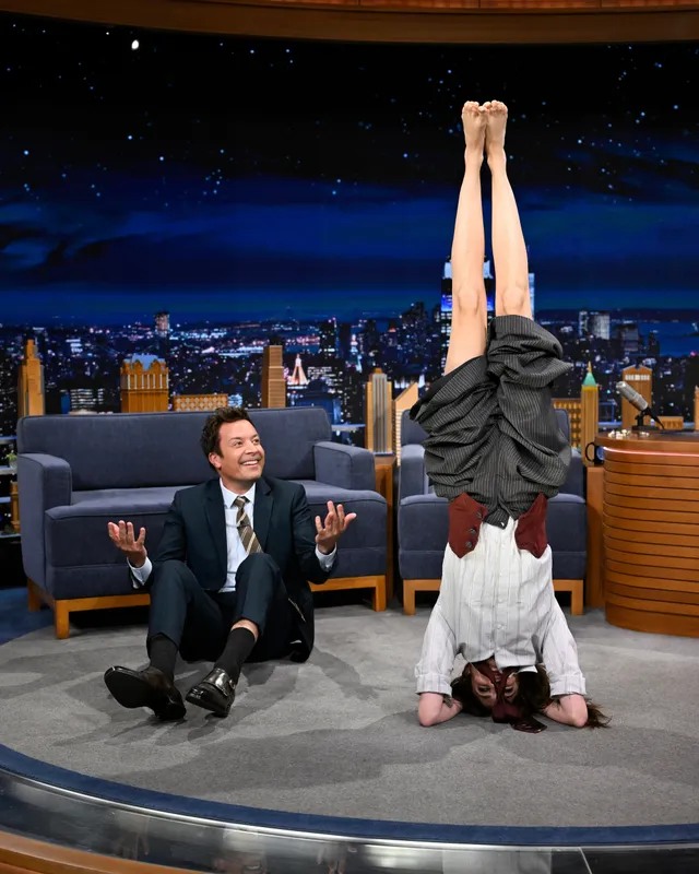 Cara Delevingne balancing upside down on a talk show set.