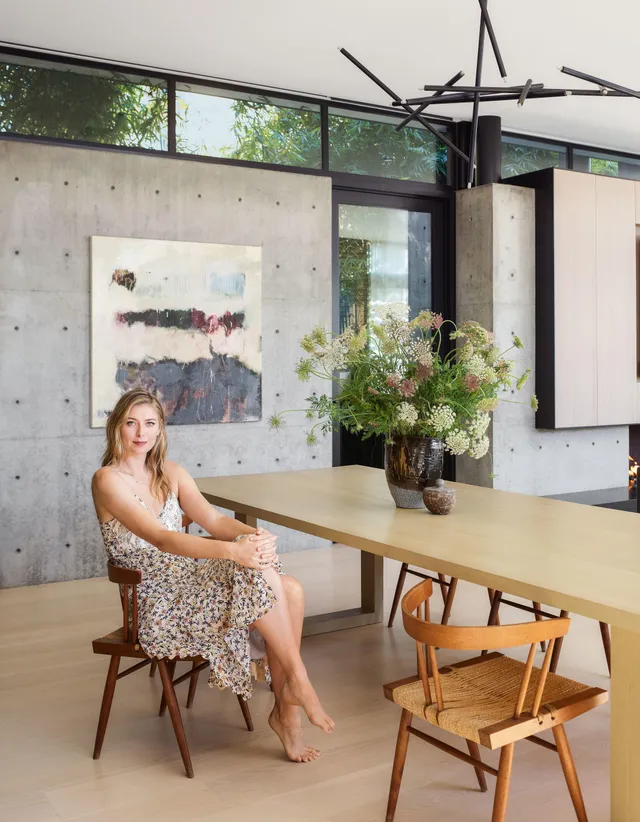 Maria Sharapova sitting barefoot at a wooden table in a bright room.
