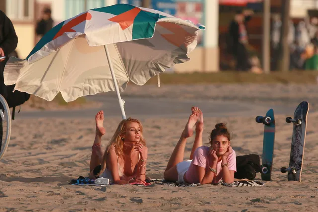 Taylor Hill relaxing barefoot beneath a beach parasol beside a companion.