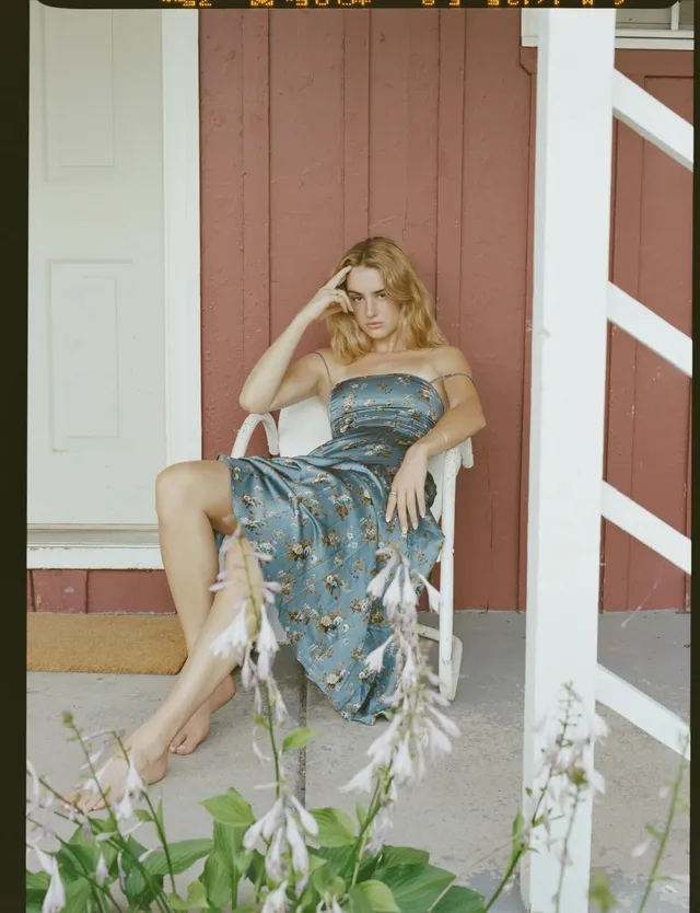 Grace Van Patten sitting on a porch in a floral dress with bare feet.