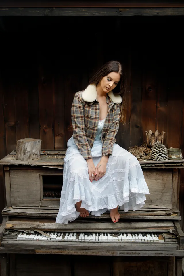 Lana Del Rey sitting barefoot on a piano in a layered skirt.