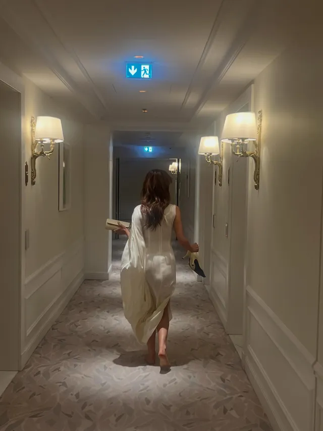 Daisy Edgar-Jones walking down a hotel corridor in a pale dress.