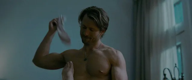 Adria Arjona with a bare foot resting against a man's chest in a film scene.