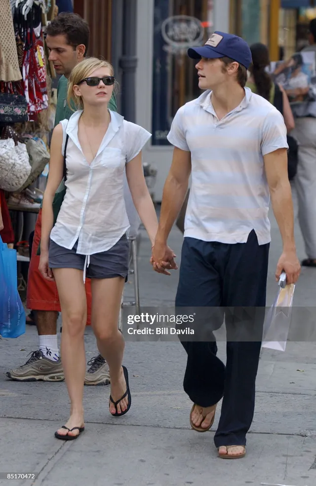 Kirsten Dunst walking outdoors in a white shirt and dark shorts.