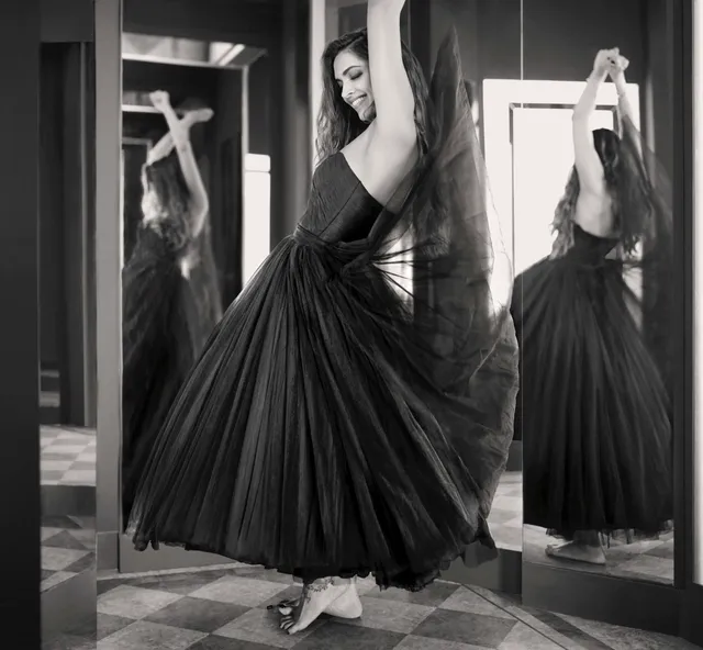 Deepika Padukone wearing embellished flat shoes beneath a long black dress during a monochrome fashion shoot.