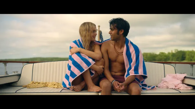 Emily Alyn Lind sitting beside a man on a boat wrapped in a striped towel.
