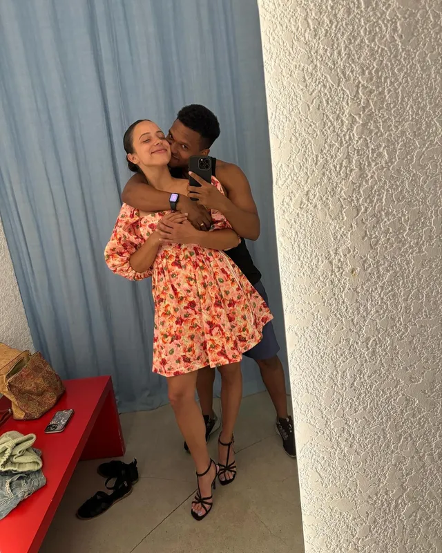 Kiana Madeira taking a mirror selfie with a man in a floral dress and black heels.