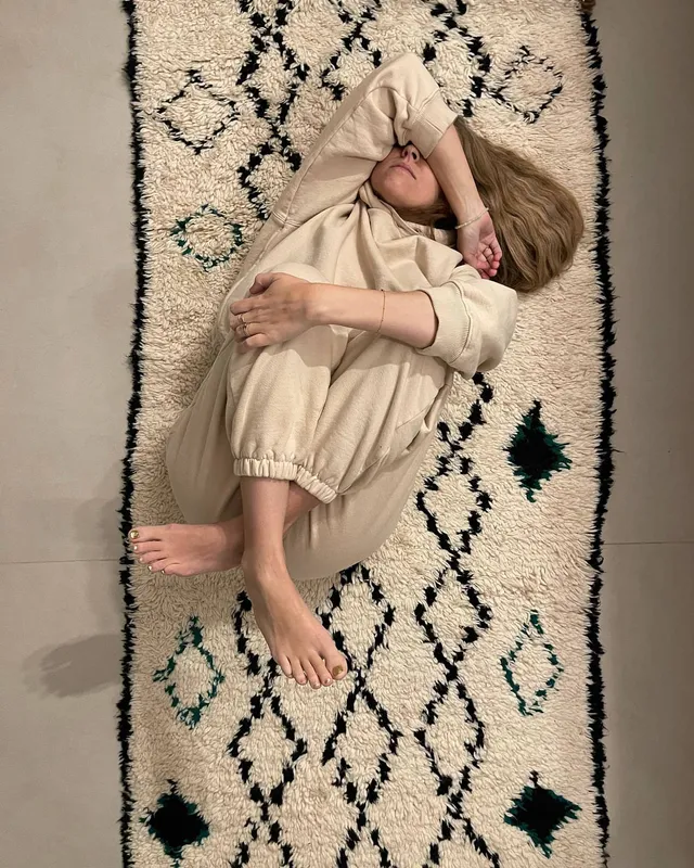 Teresa Palmer resting on a patterned rug in a light outfit.