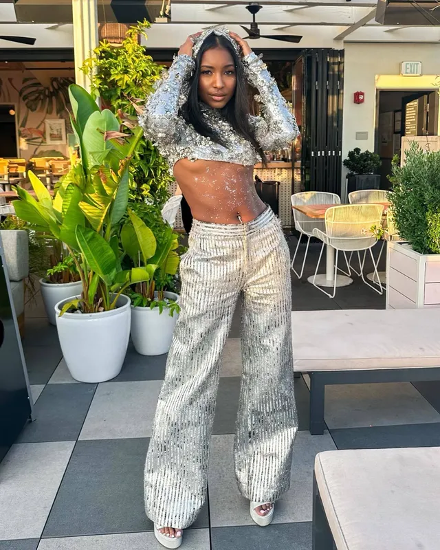 Carlacia Grant posing in a silver trouser outfit and white open-toe heels.