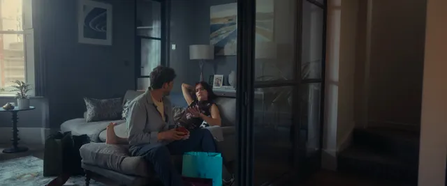 Olivia Cooke sitting on a sofa beside a man in a screen scene.