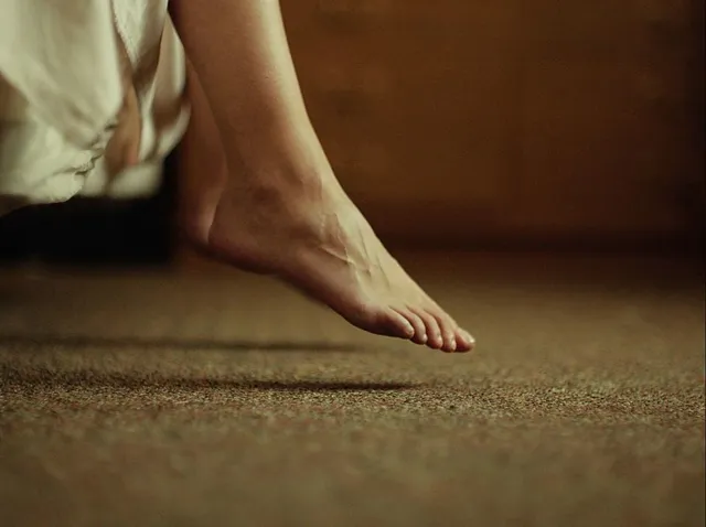 Maia Mitchell standing barefoot on carpet in a scene.