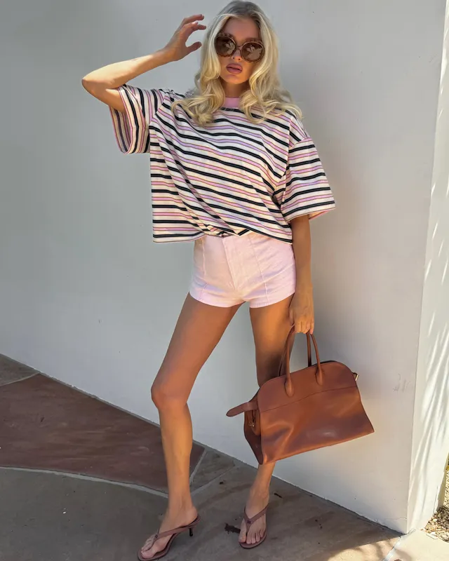 Elsa Hosk wearing pale flat sandals with a striped T-shirt and pink shorts.
