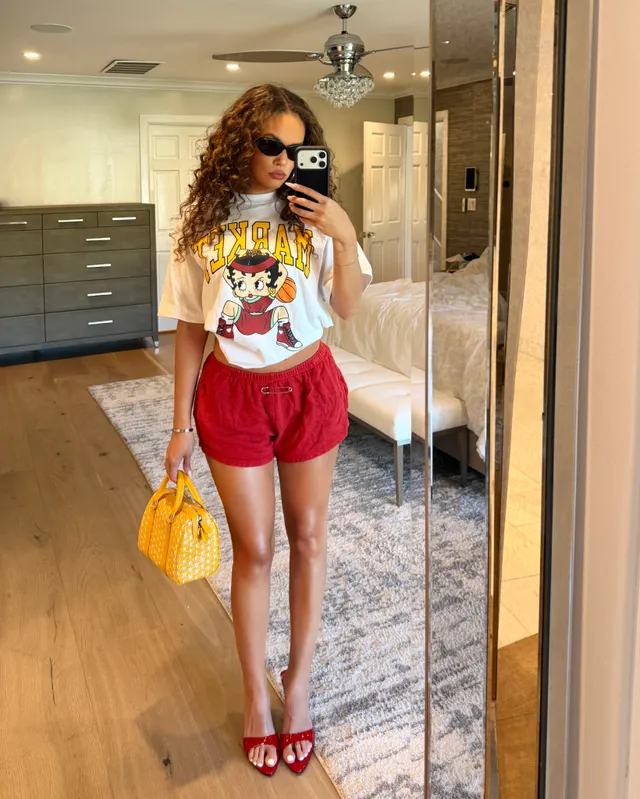 Madison Pettis taking a mirror selfie in a T-shirt, red shorts and red heels.