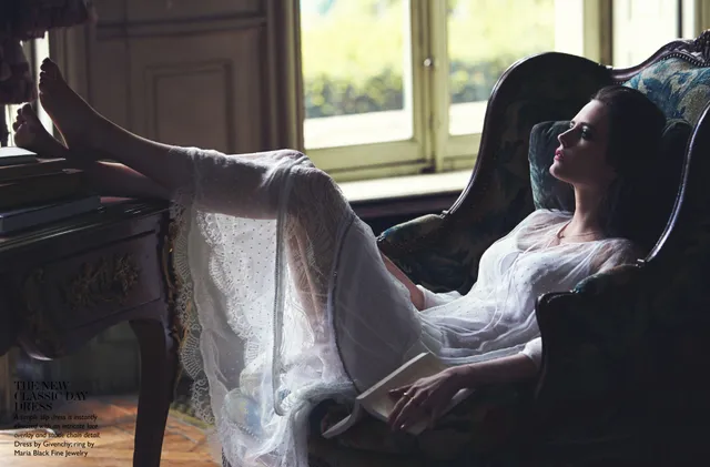 Eva Green reclining beside a desk in a flowing pale dress.