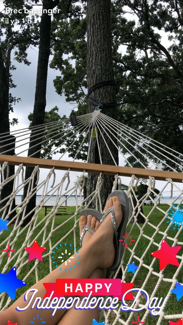 Brec Bassinger reclining outdoors in a hammock wearing flat sandals.