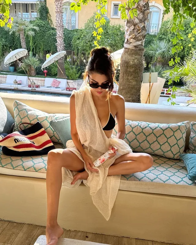 Hande Erçel sitting barefoot in a cream cover-up.