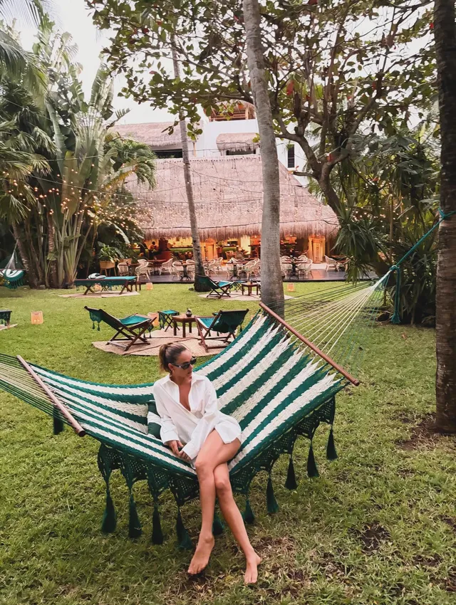 Lily James sitting barefoot in a hammock outdoors.