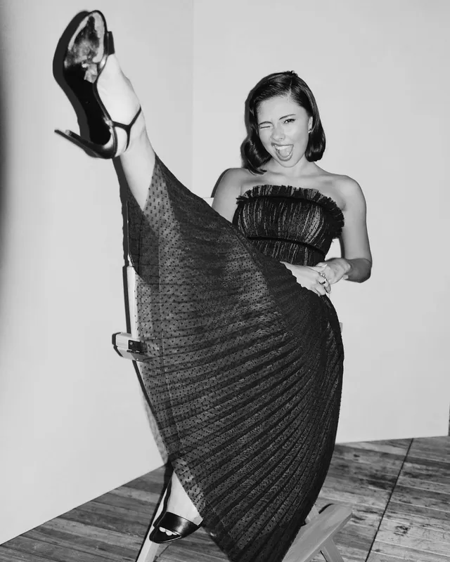 Xochitl Gomez posing in a dark dress and heels with one leg raised.