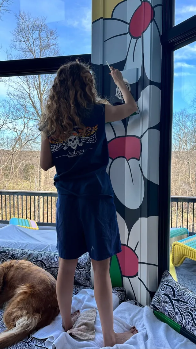Debby Ryan painting a wall beside a window.