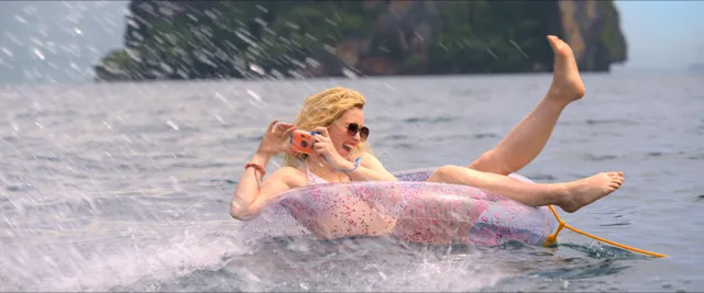 Kathryn Newton splashing in shallow water with her bare feet raised.