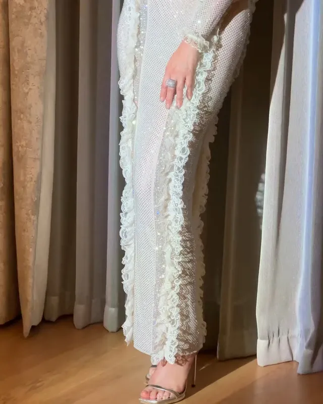 Gemma Chan wearing clear sandals beneath a long white outfit.