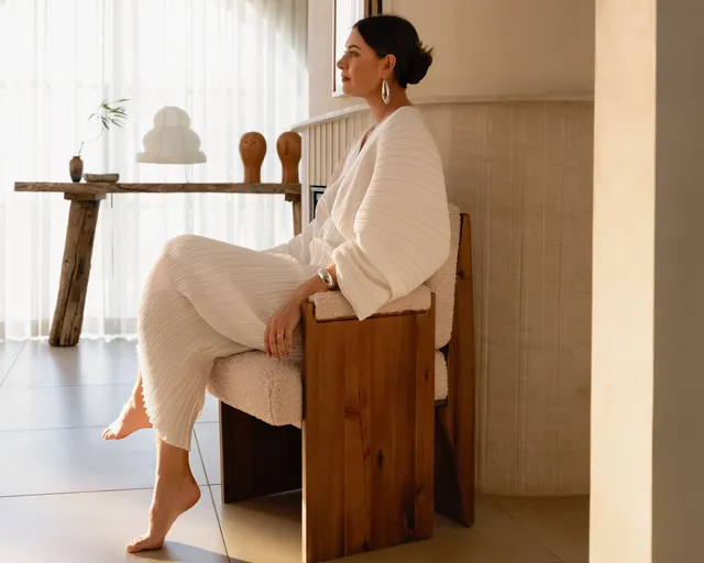 Maria Sharapova sitting barefoot in a wooden chair in a pale knit outfit.