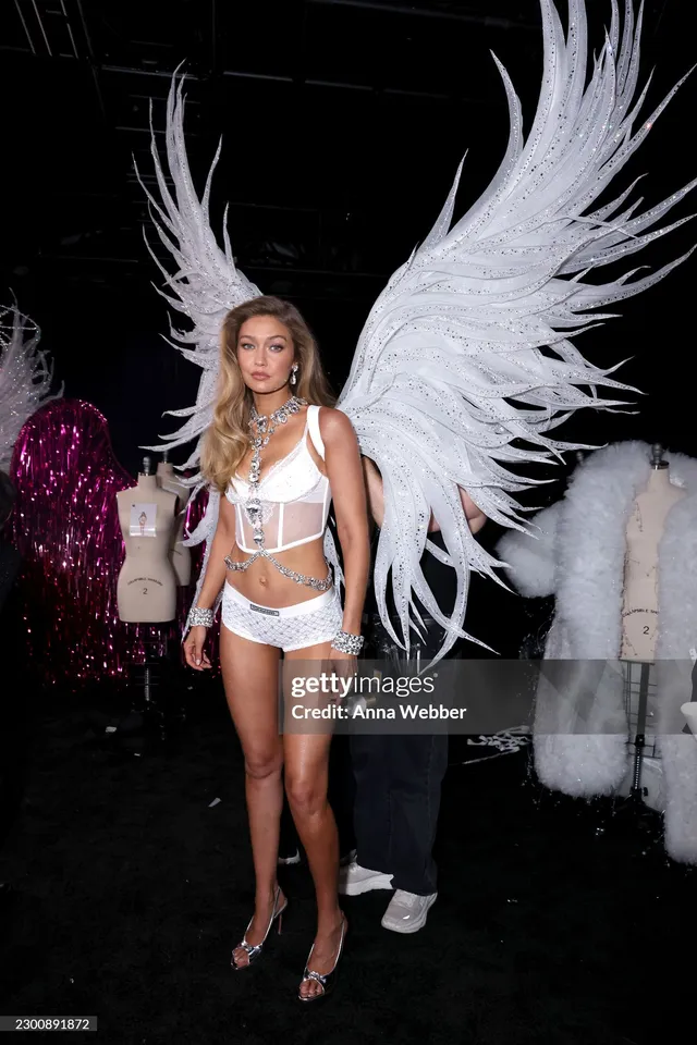 Gigi Hadid posing backstage in white wings and heels.
