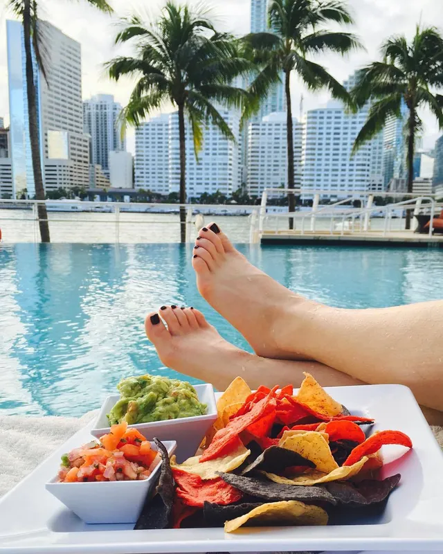 Natalie Dormer relaxing beside a pool with a tray of food.