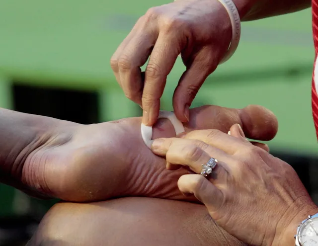 Maria Sharapova receiving treatment to the underside of her bare foot beside a tennis court.
