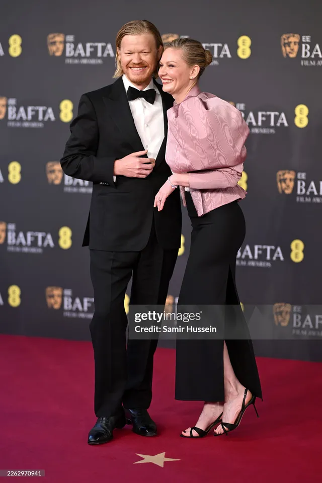 Kirsten Dunst standing with a companion in a pink jacket at an awards event.