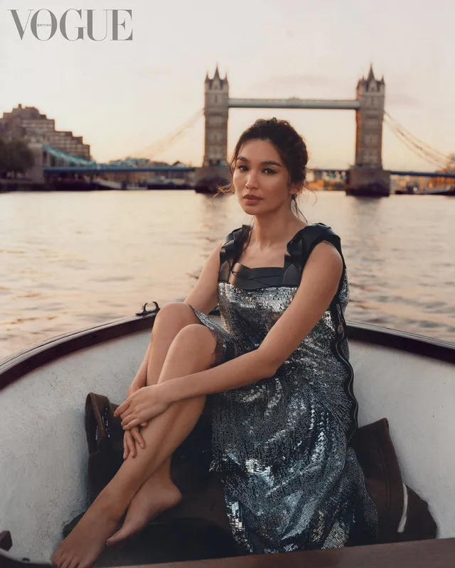 Gemma Chan sitting on a boat beside Tower Bridge.