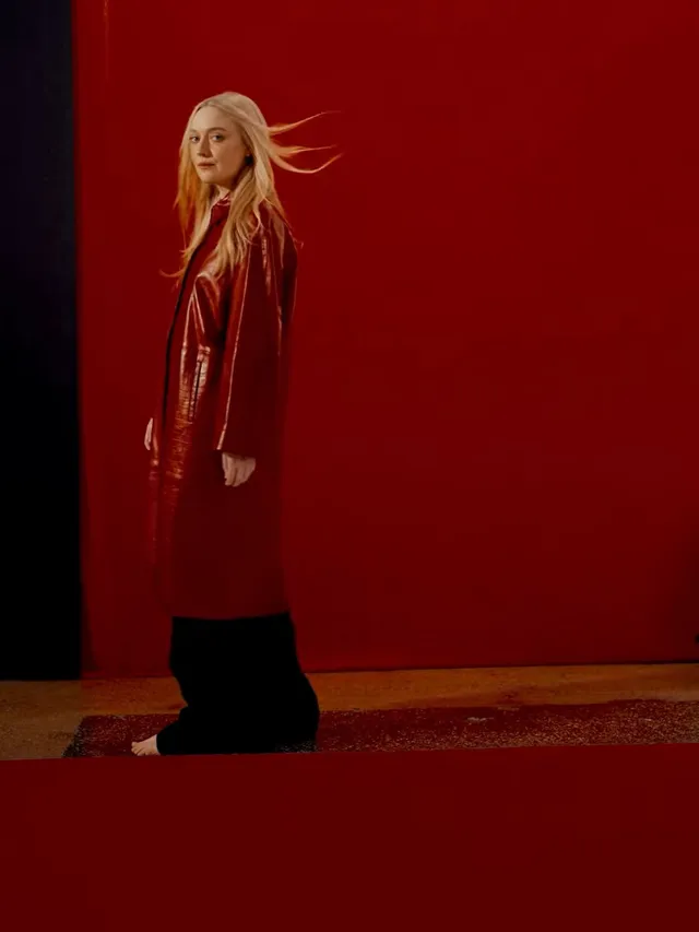 Dakota Fanning standing in a red coat against a red background.