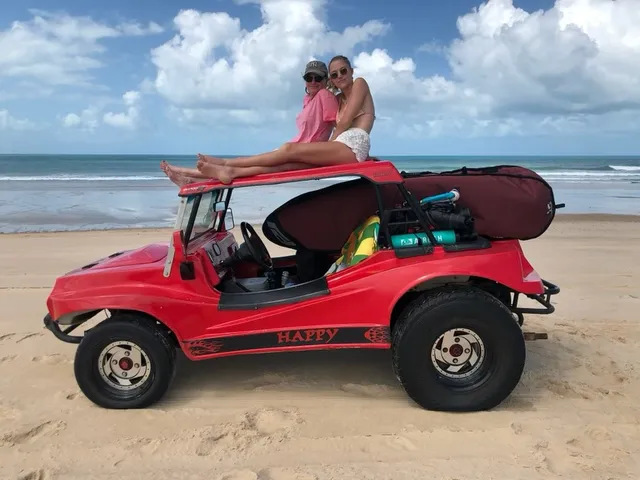 Maika Monroe sitting barefoot atop a beach vehicle with a companion.